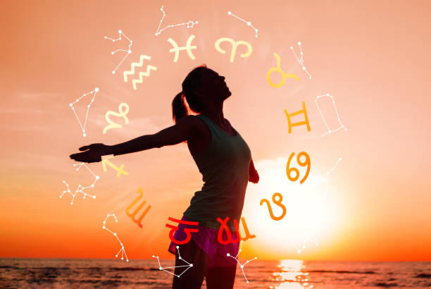 Silueta de una mujer frente al mar bajo una rueda zodiacal